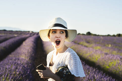 Surprised young woman with smart phone on lavender field - JCCMF03187