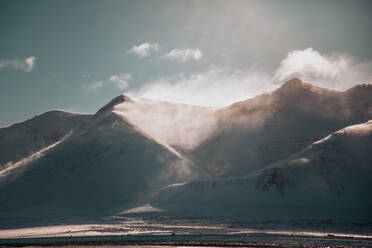 Malerischer Blick auf eine mit weißem Schnee bedeckte Berglandschaft vor grauem Himmel an einem kalten Wintertag in Island - ADSF27323