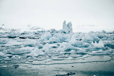 Von oben auf weiße Eisbrocken auf ruhigem Seewasser mit abgelegenen schneebedeckten Bergen und bewölktem Himmel im Hintergrund in Island - ADSF27331
