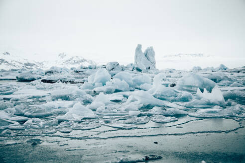Von oben auf weiße Eisbrocken auf ruhigem Seewasser mit abgelegenen schneebedeckten Bergen und bewölktem Himmel im Hintergrund in Island - ADSF27331