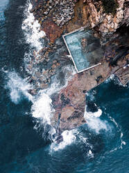 Luftaufnahme von großen Ozeanwellen, die sich über Felsen entlang des Küstenfelsenpools in Narrabeen, Sydney, Australien, brechen - AAEF09532