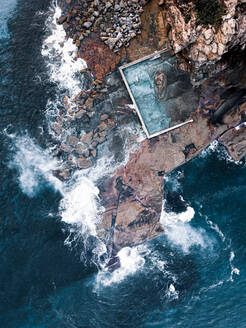 Luftaufnahme von großen Ozeanwellen, die sich über Felsen entlang des Küstenfelsenpools in Narrabeen, Sydney, Australien, brechen - AAEF09532