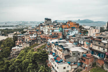 Luftaufnahme von dicht gepackten farbigen Häusern von Santo Amaro Hillside Favela, Niteroi in der Ferne, Rio De Janeiro, Brasilien - AAEF09549