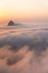 Luftaufnahme über eine Decke von niedrigen Wolken von Sugarloaf Mountain Peak bei Sonnenaufgang in Rio de Janeiro, Brasilien - AAEF09662