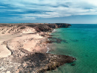 Luftaufnahme des einsamen Strandes mit einem Mann, der an der Küste von Playa del Pozo, Lanzarote, Spanien, entlangläuft. - AAEF09734