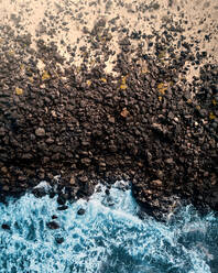 Luftaufnahme eines felsigen Strandes aus Lava und Sand, umgeben von rauem Wasser in Famara, Lanzarote, Spanien. - AAEF09752