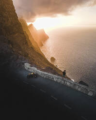 Luftaufnahme einer Person, die mit ihrem Motorrad entlang der Straße eine Pause macht und die Landschaft bei Sonnenuntergang in der Nähe von La Aldea de San Nicol√°s, Kanarische Insel, Spanien, betrachtet. - AAEF09838