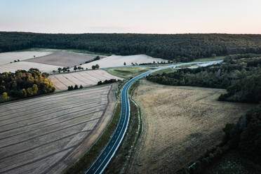 Luftaufnahme einer Straße, die sich durch Wälder und Felder von G√∂ttingen, Deutschland, schlängelt. - AAEF09848