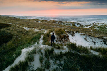 Luftaufnahme eines Mannes, der bei Sonnenuntergang auf der Insel Terschelling, Friesland, Niederlande, auf den Dünen steht und das Meer überblickt. - AAEF09904