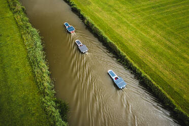 Luftaufnahme von Booten mit Solarzellen, die durch das Ackerland von Schettens, Friesland, Niederlande, fahren. - AAEF09932