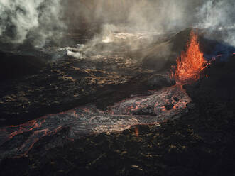 Luftaufnahme eines aus dem Krater rauchenden Vulkans, Blick auf aus dem Krater ausbrechendes Magma mit Berglandschaft im Hintergrund, Grindav√≠k, Südliche Halbinsel, Island. - AAEF09947