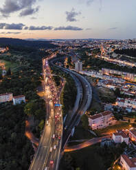 Luftaufnahme der Autobahn auf dem Monsanto-Hügel bei Sonnenuntergang mit der Skyline von Lissabon im Hintergrund, Alc√¢ntara, Lissabon, Portugal. - AAEF09970