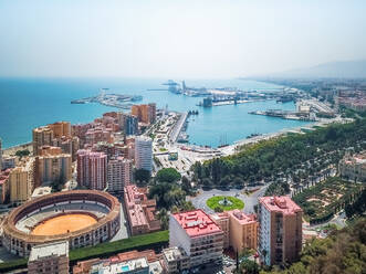 Aerial view of La Malagueta Bullring with the tall building around it and the port of Malaga in the background, Andalusia, Spain. - AAEF09994