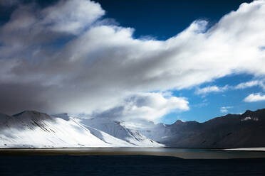 Atemberaubender Blick auf einen wolkenverhangenen Himmel über einem verschneiten Bergkamm und einem ruhigen See an einem Wintertag in Island - ADSF27335