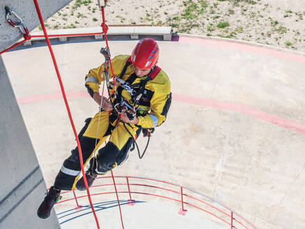 Berufsfeuerwehrmann in Uniform hängt an Seilen, während er das Klettern an einer Wand trainiert - ADSF27350