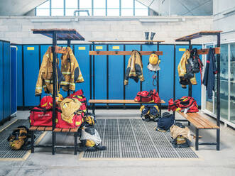 Leerer Umkleideraum in der Feuerwehr mit aufgehängten Uniformen und blauen Spinden - ADSF27352