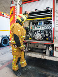 Anonymous Equipped fireman standing and using an water engine into fire truck - ADSF27360