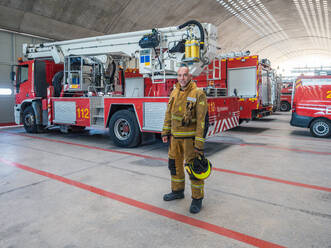 Berufsfeuerwehrmann steht in der Nähe des Feuerwehrautos und schaut in die Kamera - ADSF27361