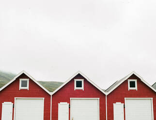 Amazing view of gray sky over three red sheds in small settlement in Lapland - ADSF27437