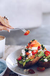 Frische leckere Bruschetta mit Gemüse und Frischkäse auf Tisch und Gabel mit Tomate in der Luft - ADSF27473