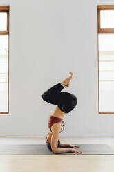 Young pretty woman in sportswear practicing yoga asana on floor in training room - ADSF27502