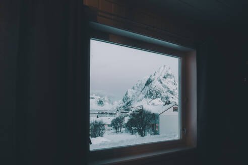 Blick aus dunklem Raum auf Gebäude in der Nähe von Steinhügeln im Schnee an der Küste in der Nähe von Wasser im Winter in Arktis Island - ADSF27518