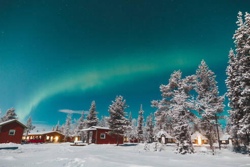 Malerische Ansicht der Häuser der kleinen Stadt im Schnee in der Nähe von Bäumen und wunderbare Polarlichter am Himmel in Arctic Island - ADSF27527