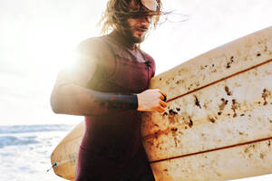 Surfer Mann im Neoprenanzug läuft mit Surfbrett am Strand bei Sonnenaufgang - ADSF27571