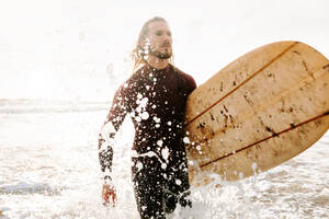 Surfer Mann im Neoprenanzug läuft mit Surfbrett am Strand bei Sonnenaufgang - ADSF27572