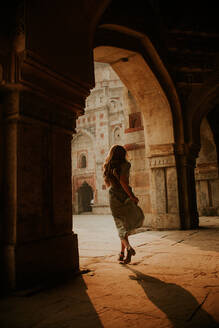 Full body back view of anonymous female tourist running under arched passage of Muhammad Shah Sayyid Tomb at Lodhi Garden in New Delhi - ADSF27605