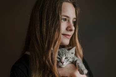 Dreamy nachdenklich Teenager-Mädchen hält flauschige niedliche Katze auf braunem Hintergrund im Studio - ADSF27609