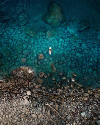 Luftaufnahme einer Person im Kajak, umgeben von kristallklarem Wasser in der Nähe eines felsigen Strandes in Caminia, Kalabrien, Italien. - AAEF10038