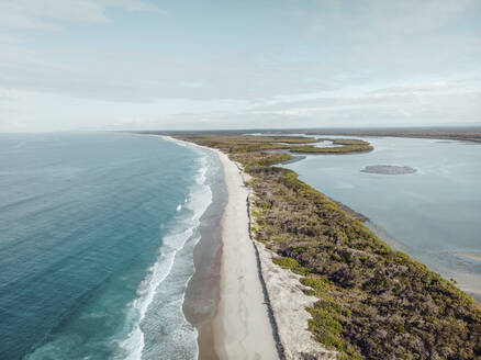 Luftaufnahme von drei kleinen Menschen, die an einem Strand mit Wasser auf zwei Seiten spazieren gehen, Bribie Island, Queensland, Australien. - AAEF10080