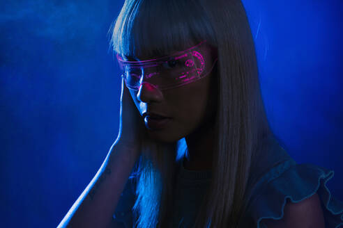 Junge Frau mit futuristischer rosa Brille vor blauem Hintergrund - EIF01763