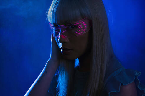 Young woman with futuristic pink eyeglasses against blue background - EIF01763