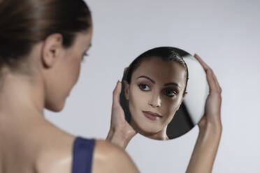 Woman looking at mirror reflection against white background - EIF01773