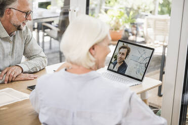 Männliche und weibliche Geschäftsleute führen ein Videogespräch mit einem Kollegen auf einem Laptop im Heimbüro - UUF24019