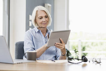 Businesswoman using digital tablet at desk in home office - UUF24039