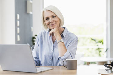 Businesswoman with hand on chin at desk in home office - UUF24041