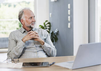 Thoughtful male professional with hands clasped at home office - UUF24045