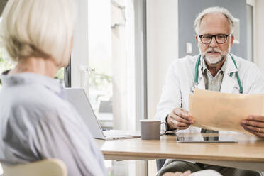 Male doctor examining medical report at desk - UUF24059