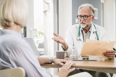 Mature male doctor advising female patient at desk - UUF24060