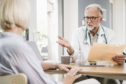 Reifer männlicher Arzt, der eine Patientin am Schreibtisch berät - UUF24060