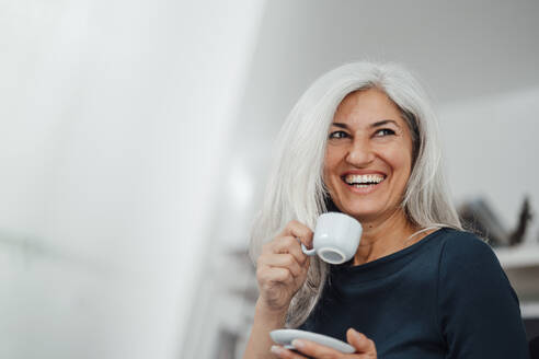 Female professional laughing while having coffee at office - JOSEF05041