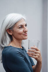 Geschäftsfrau schaut weg, während sie an der Wand im Büro Wasser trinkt - JOSEF05057