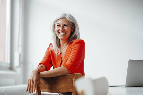 Happy female professional looking away while leaning on chair at office - JOSEF05081