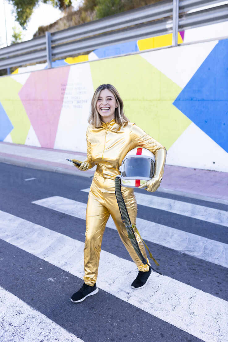 Smiling young woman in astronaut costume crossing street stock photo