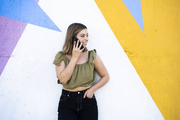 Frau mit Hand in der Tasche, die vor einer Wand mit ihrem Smartphone telefoniert - DAMF00846