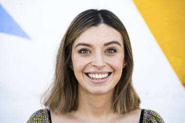 Woman with brown eyes smiling in front of wall - DAMF00849