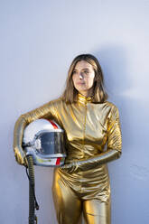 Young woman holding space helmet while standing in front of white wall - DAMF00857